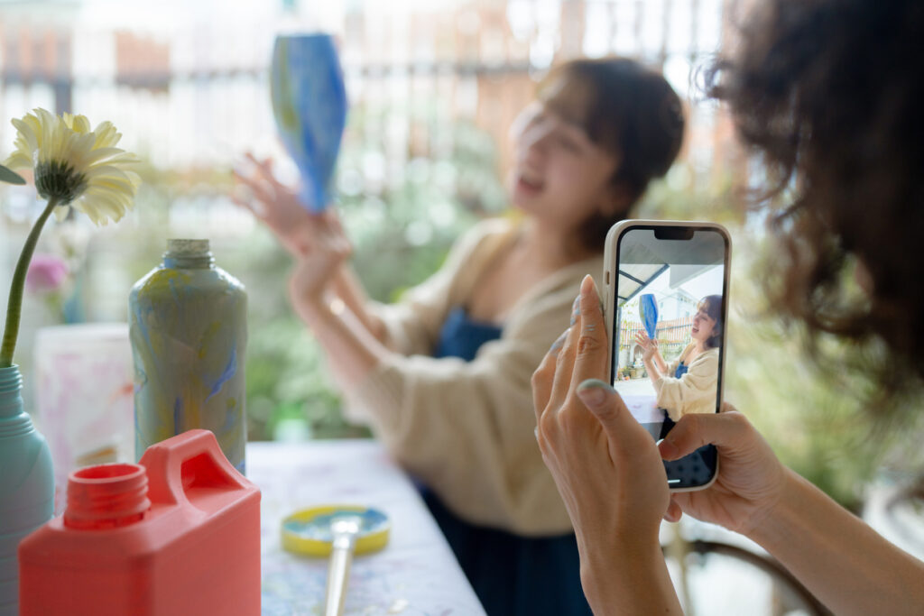 Woman takes a video on her phone of another woman displaying a vase