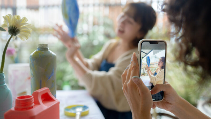 Woman takes a video on her phone of another woman displaying a vase