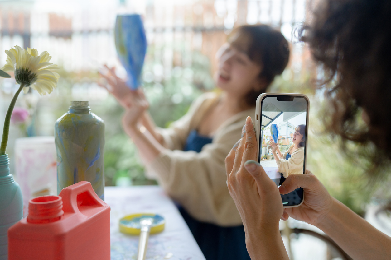 Woman takes a video on her phone of another woman displaying a vase